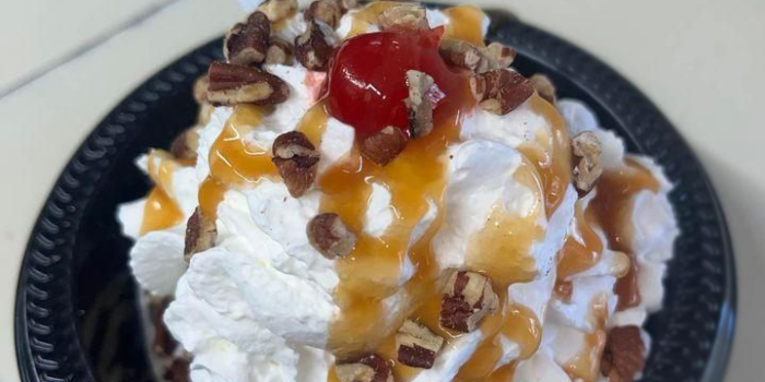 r0dc-dessert-Kool-Kone-2023-02-5 Ice cream sundae in a blue bowl topped with whipped cream, walnuts, caramel drizzle, and a cherry.
